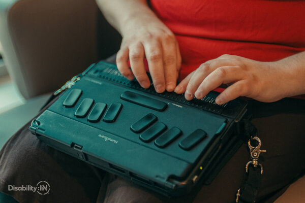 Des mains sur un bloc-notes Braille posé sur les jambes de la personne assise.